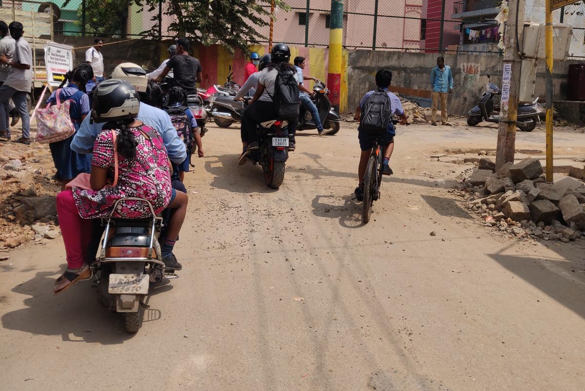 School children walking and cycling on a street without footpaths or bicycle lanes in Bengaluru.