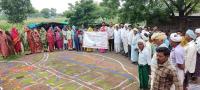 People stand around a rangoli map on the ground