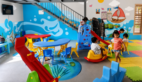 Brightly colored anganvadi with slides, climbing structures, and children playing.