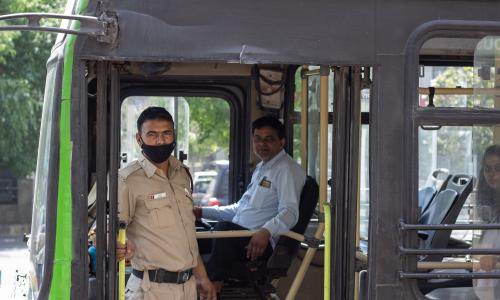 A bus driver as seen from outside the door of the bus while a police man stands inside