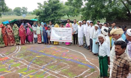 People stand around a rangoli map on the ground